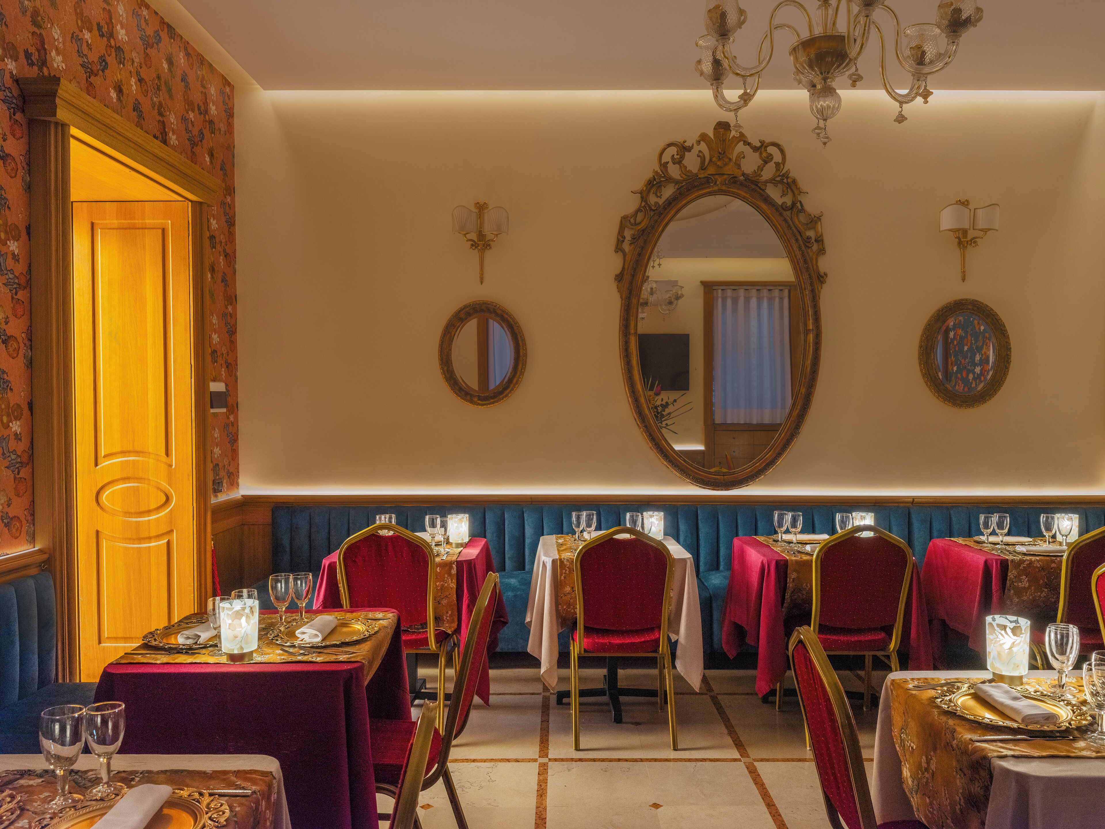 A dining area with multiple tables, each set with red and gold tablecloths, and chairs with gold frames.
