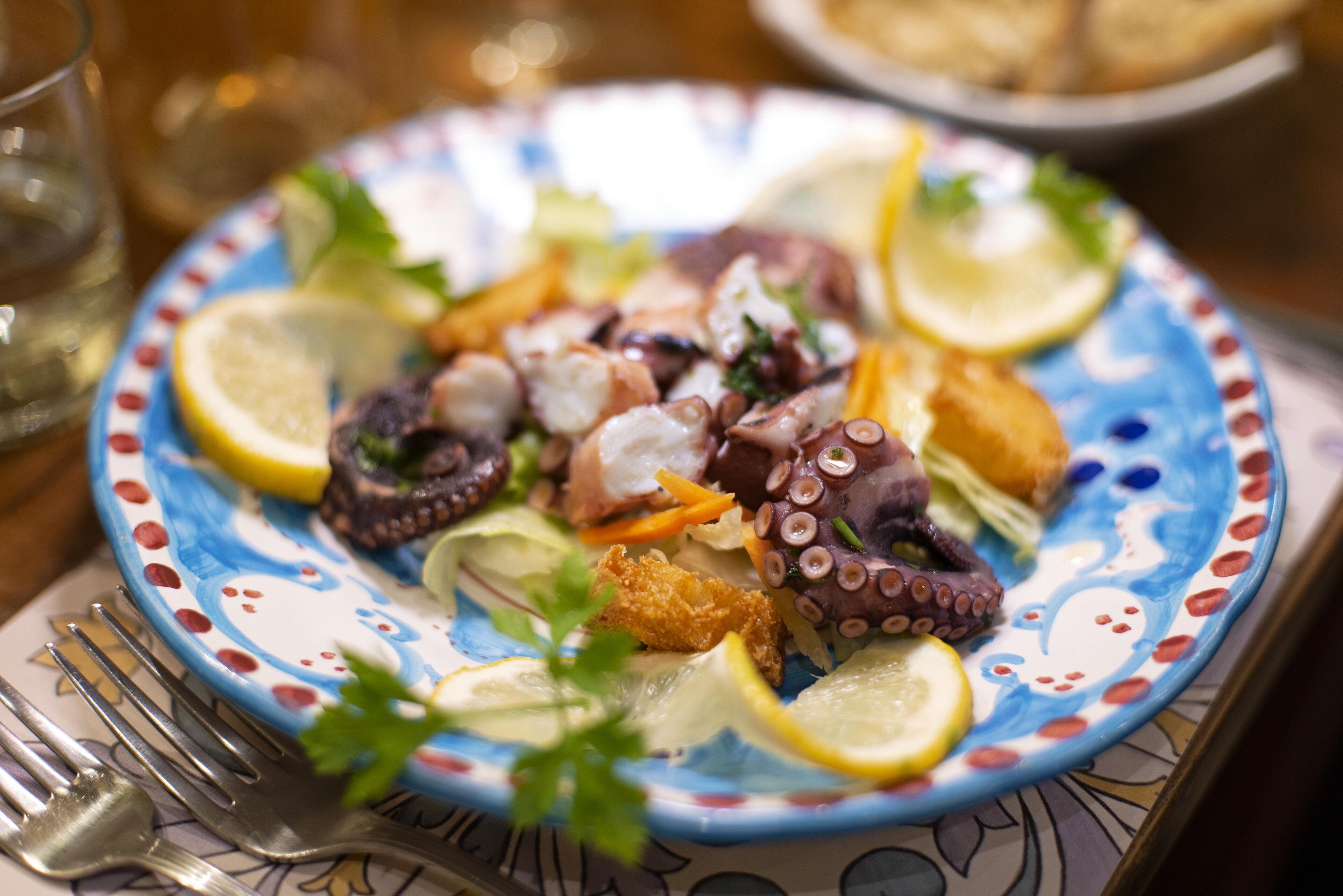 A plate of food with octopus, lemon slices, and parsley.