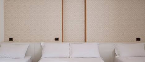 Een hotelkamer met twee bedden, een groot raam en een effen wand met een subtiel patroon.