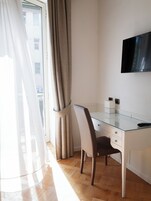 Una habitación moderna con un escritorio de vidrio, una silla, un televisor de pantalla plana y un ventanal con cortinas.