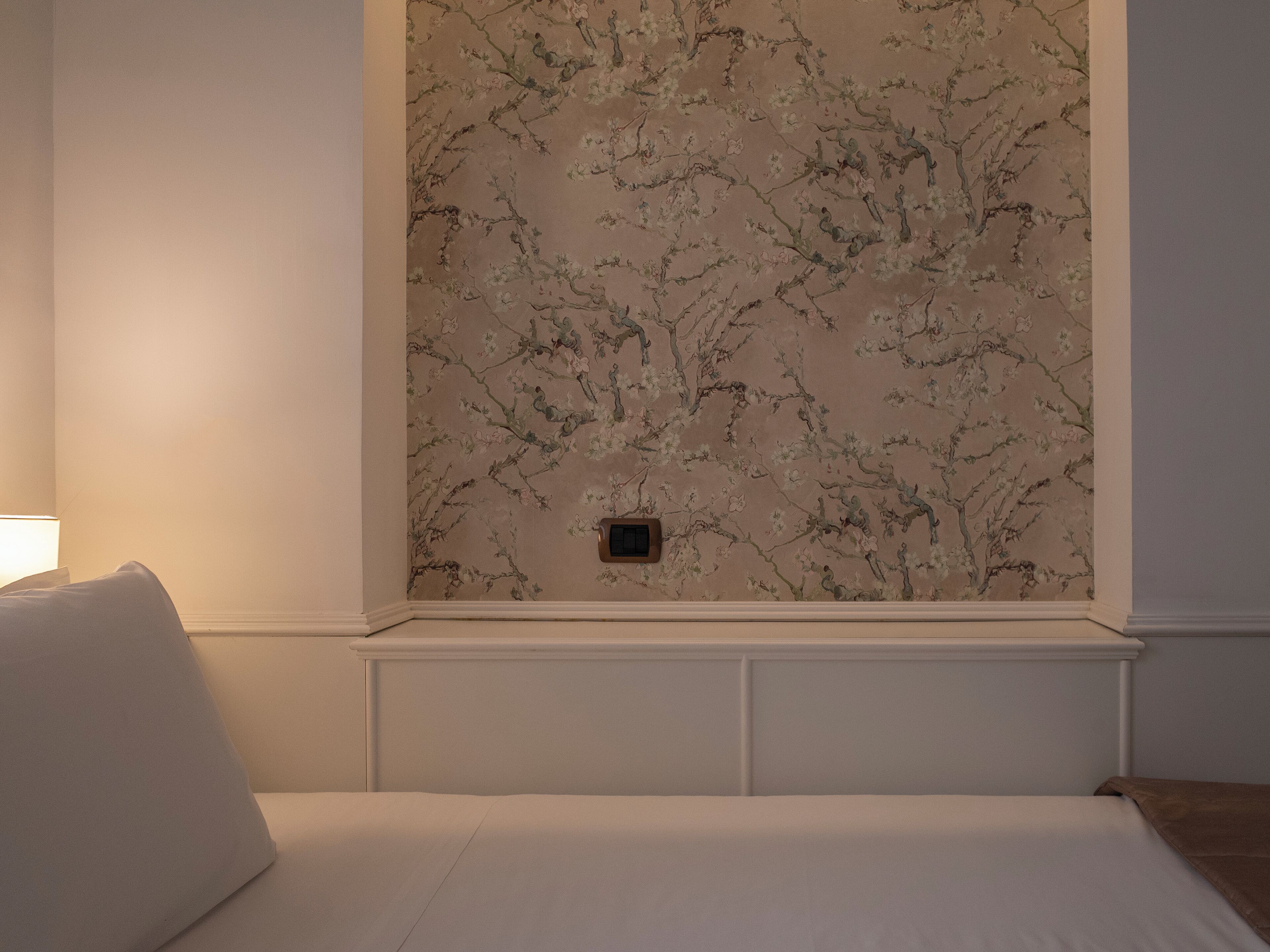Une chambre à coucher avec un lit, une table de chevet et un mur recouvert d’un papier peint à motifs floraux.
