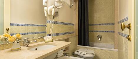 A bathroom with a sink, mirror, hairdryer, and a bathtub.