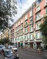A row of colorful buildings with balconies, some with plants, and a street in front.