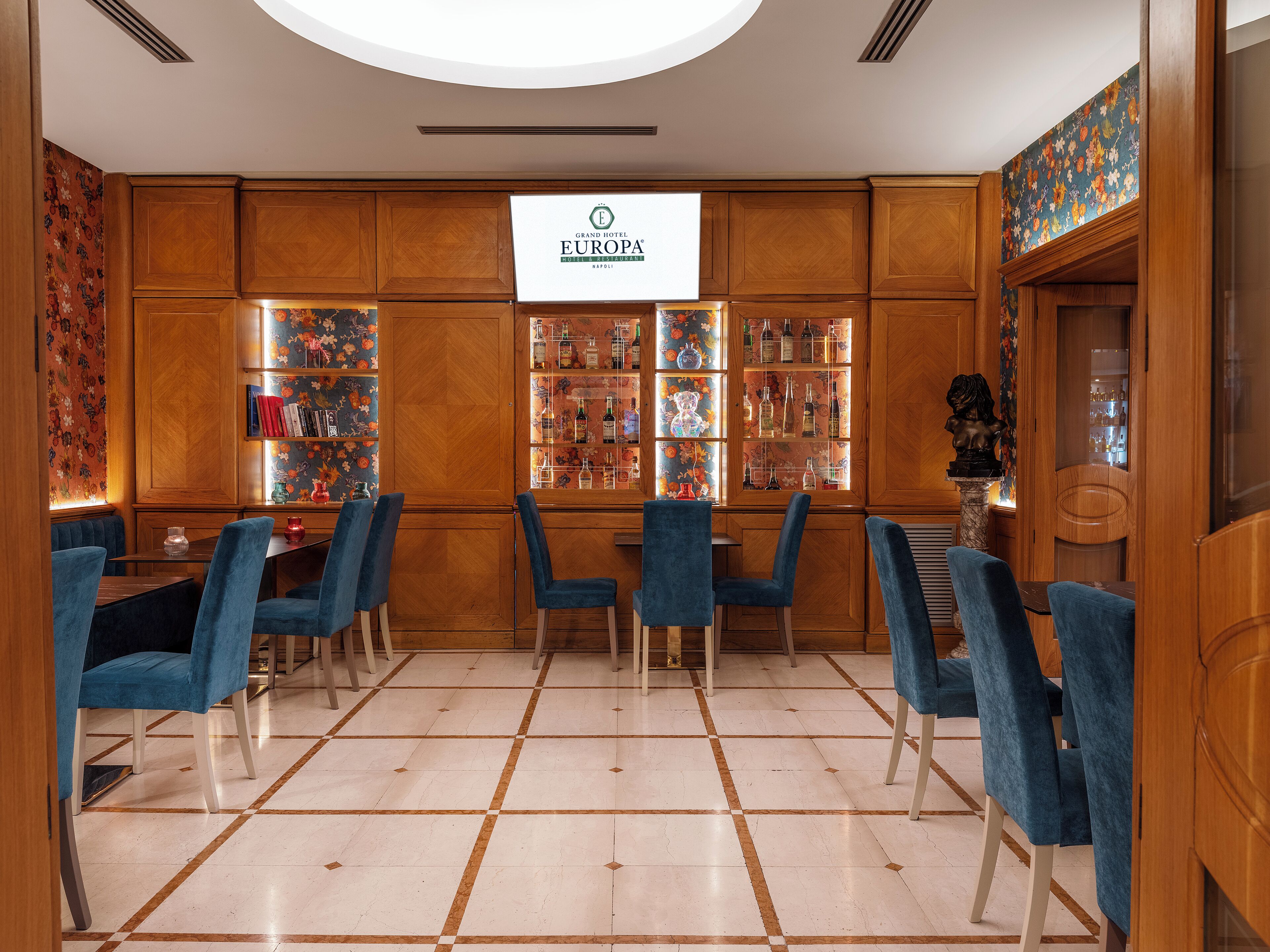 A bar area with wooden cabinets, blue chairs, and a tiled floor.