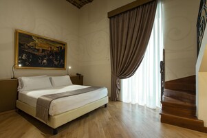 Habitación de hotel con una cama grande, un cuadro en la pared, una escalera de madera y una ventana con cortinas.
