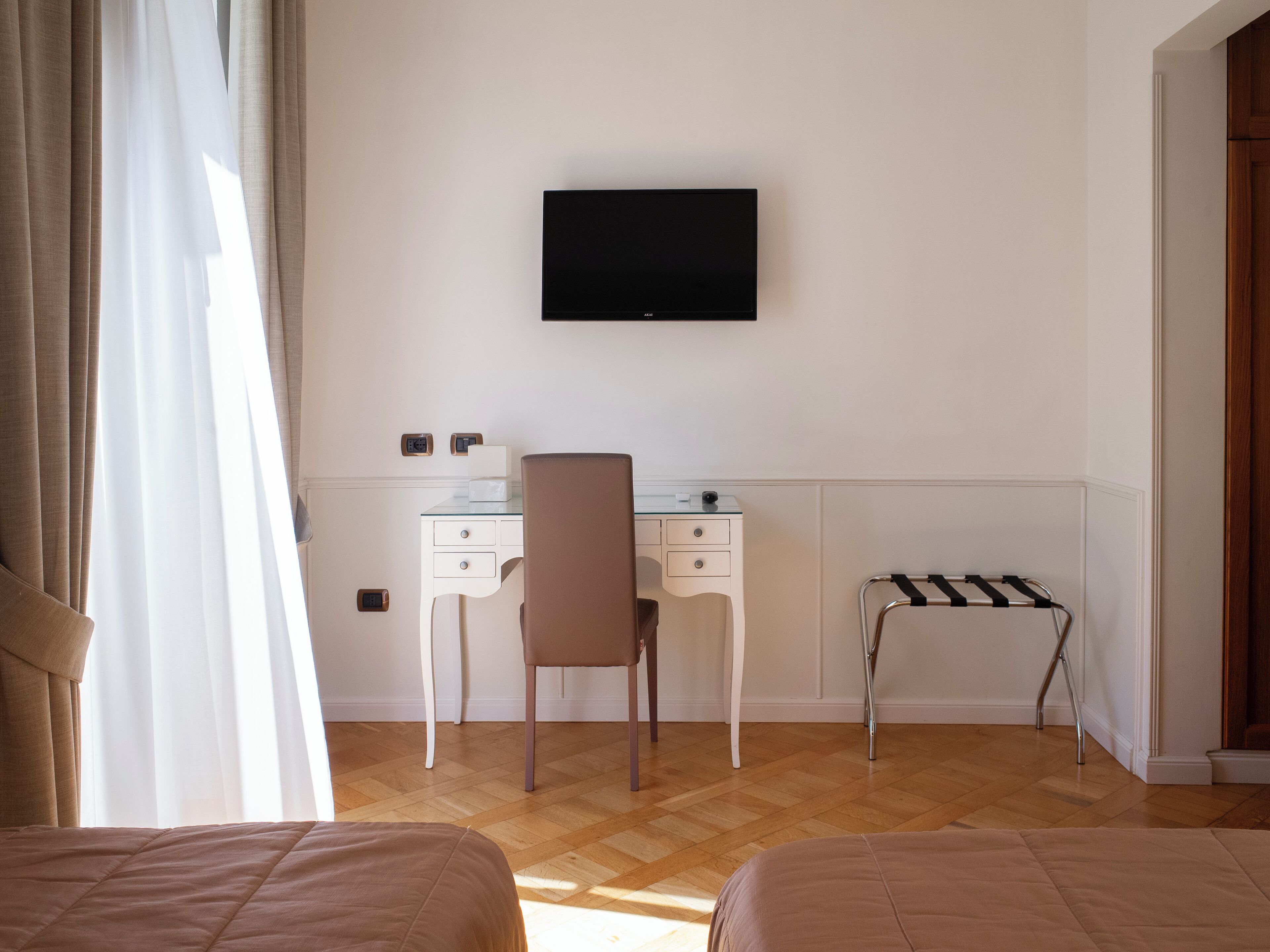 Habitación de hotel con cama, escritorio, silla, televisor, toallero y ventana con cortinas.