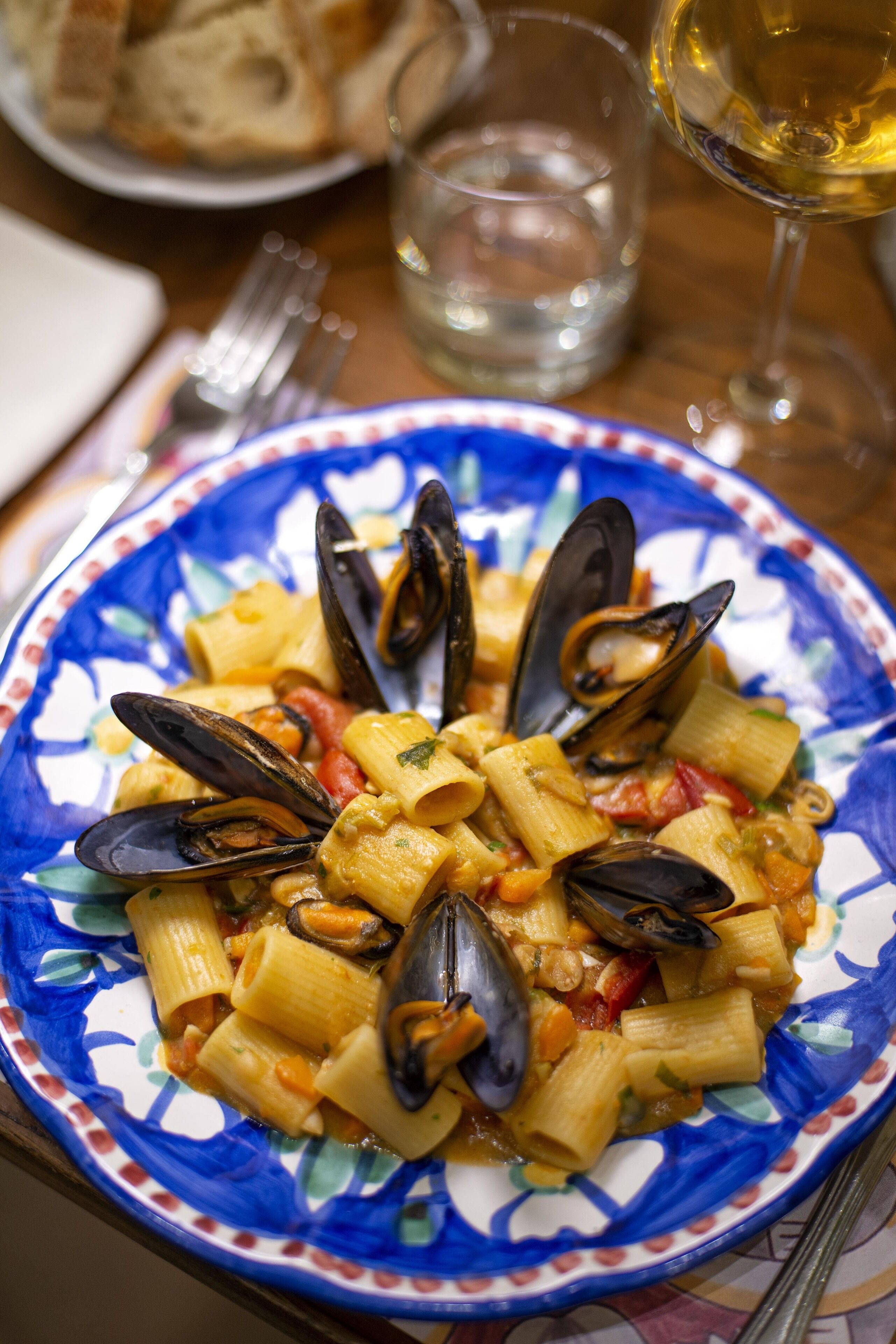 Un piatto di pasta con cozze, un bicchiere di vino bianco e una forchetta su un tavolo.