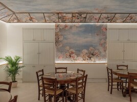 Een eethoek met een ronde tafel en houten stoelen, een kamerplant en een bloemenmuur.