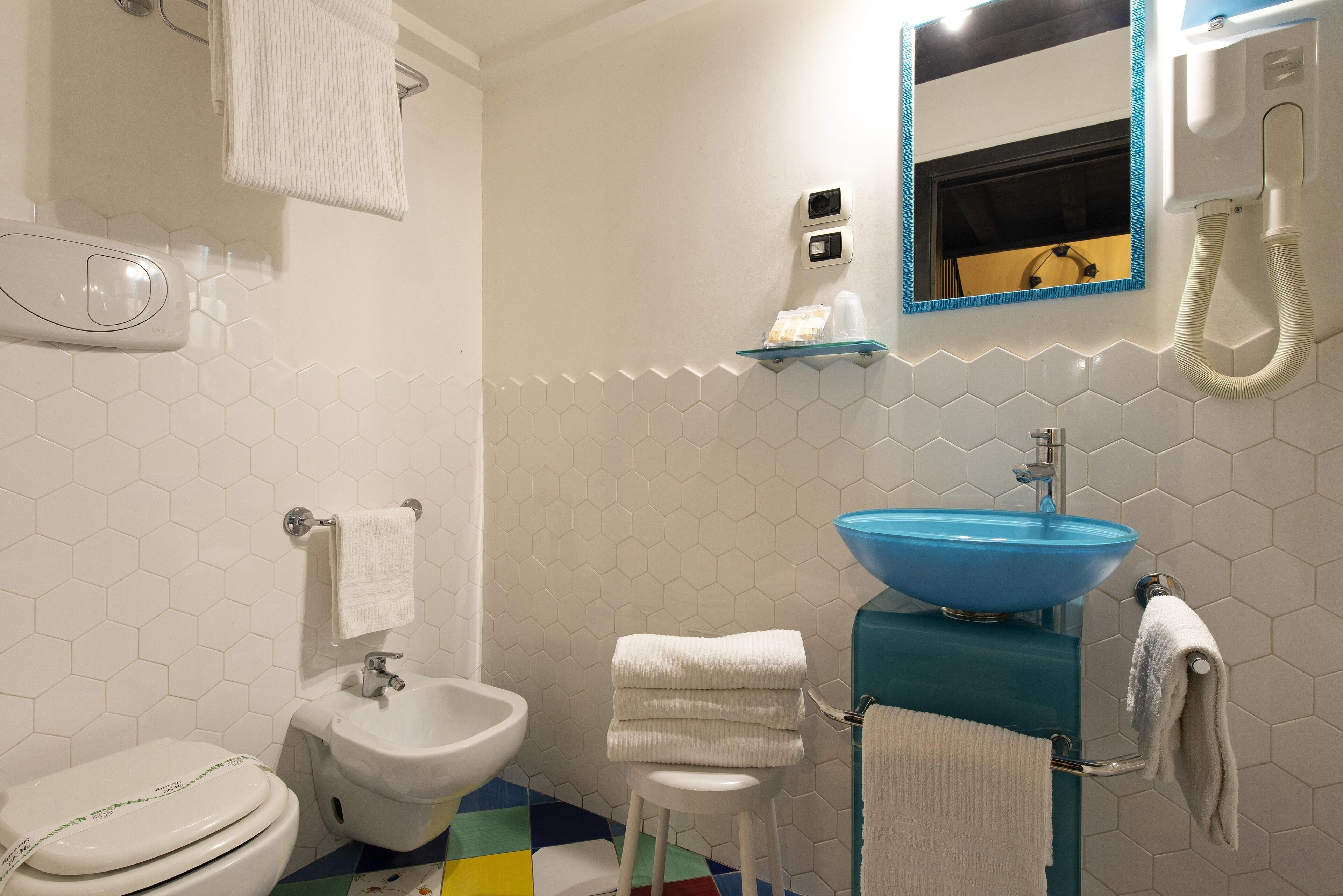 A bathroom with a white toilet, a bidet, a sink with a blue basin, and a mirror with a blue frame.