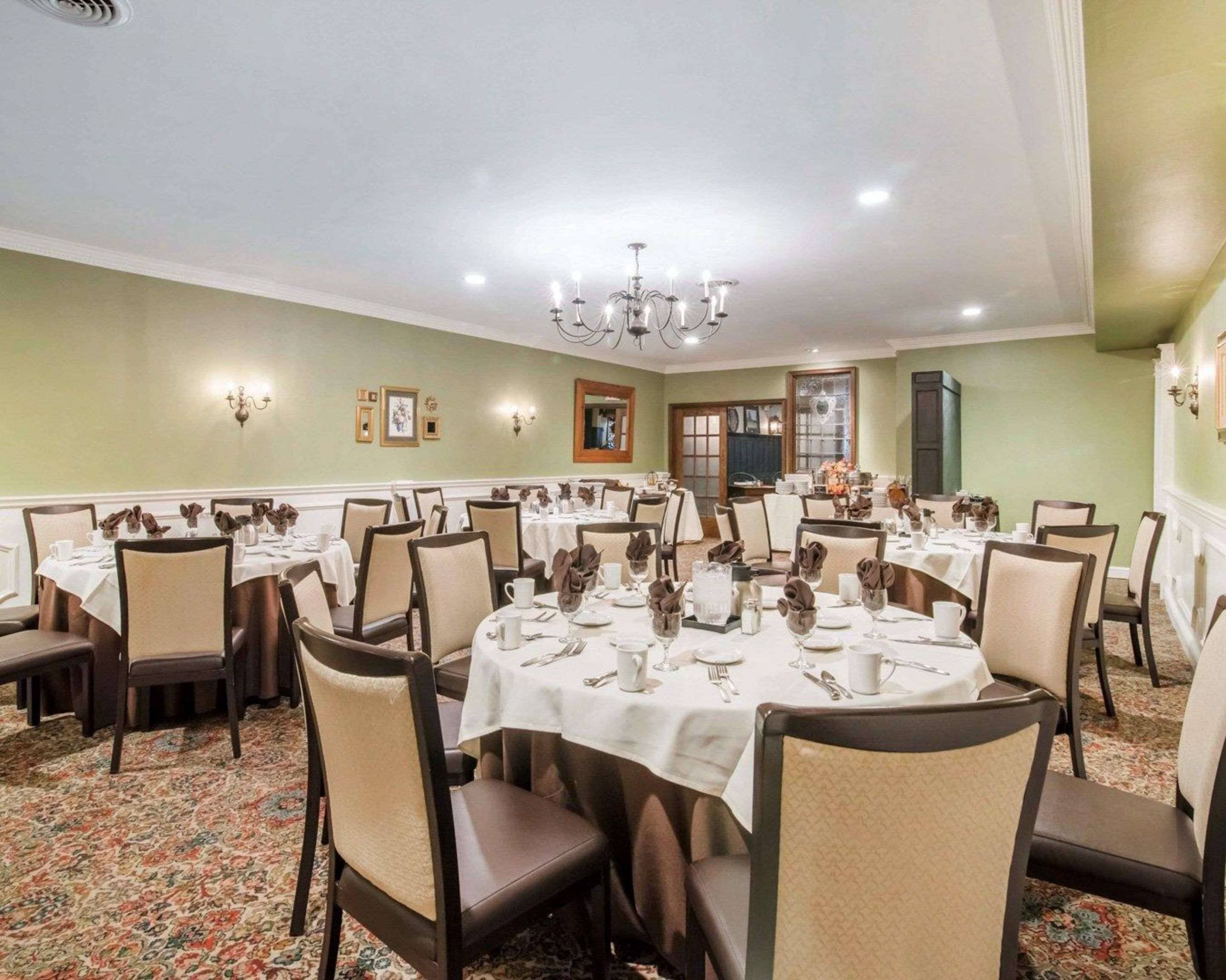 Een ruime balzaal met ronde tafels gedekt voor een diner, met witte tafellakens en netjes geplaatste bestek.