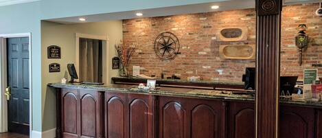 A reception area with a brick wall, a large clock, and a wooden reception desk.