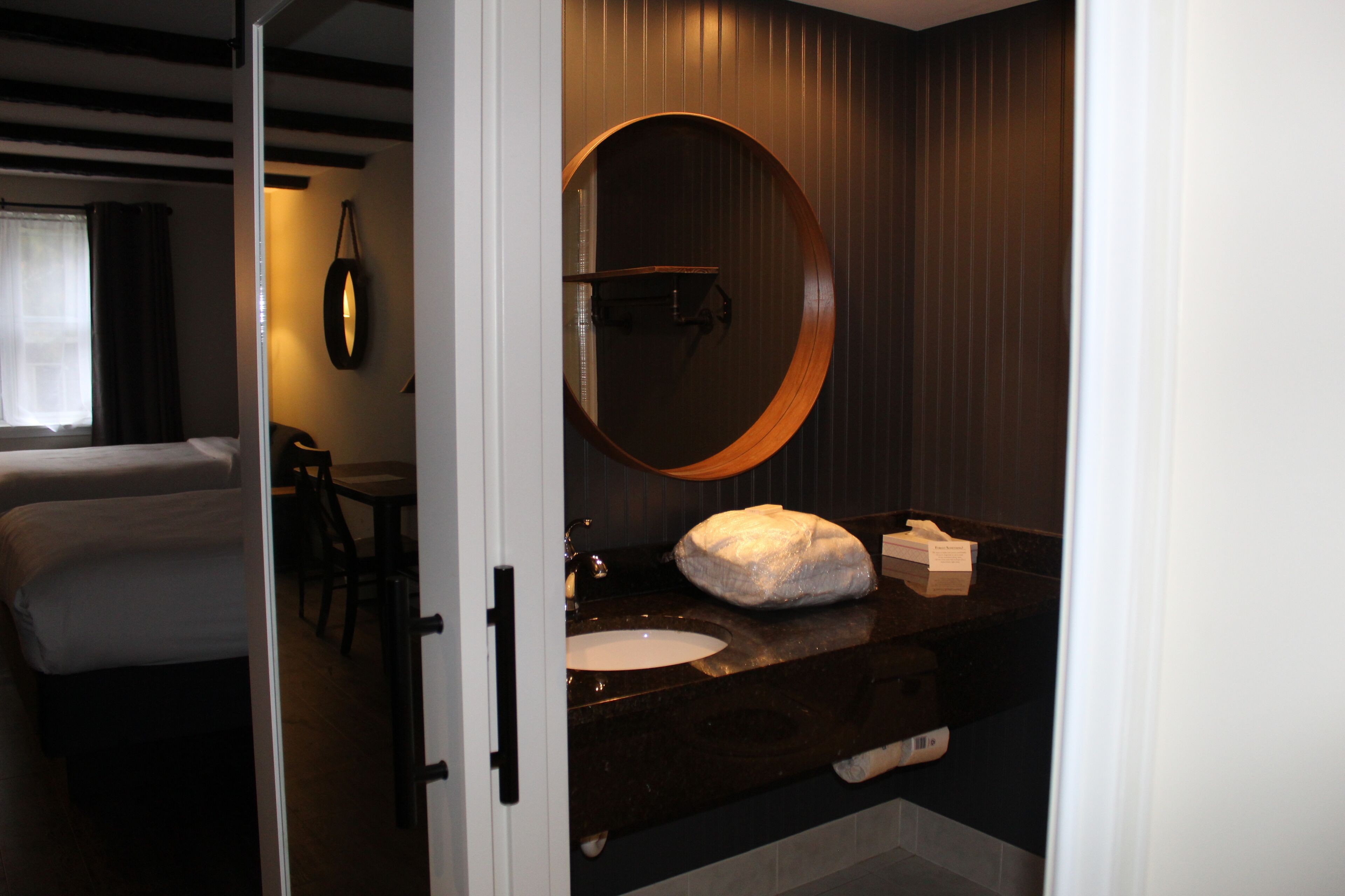 A hotel room with a bed, a round mirror, a sink, and a chair.