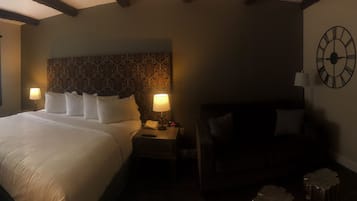 A hotel room with a large bed, two bedside lamps, a clock on the wall, and a window with curtains.