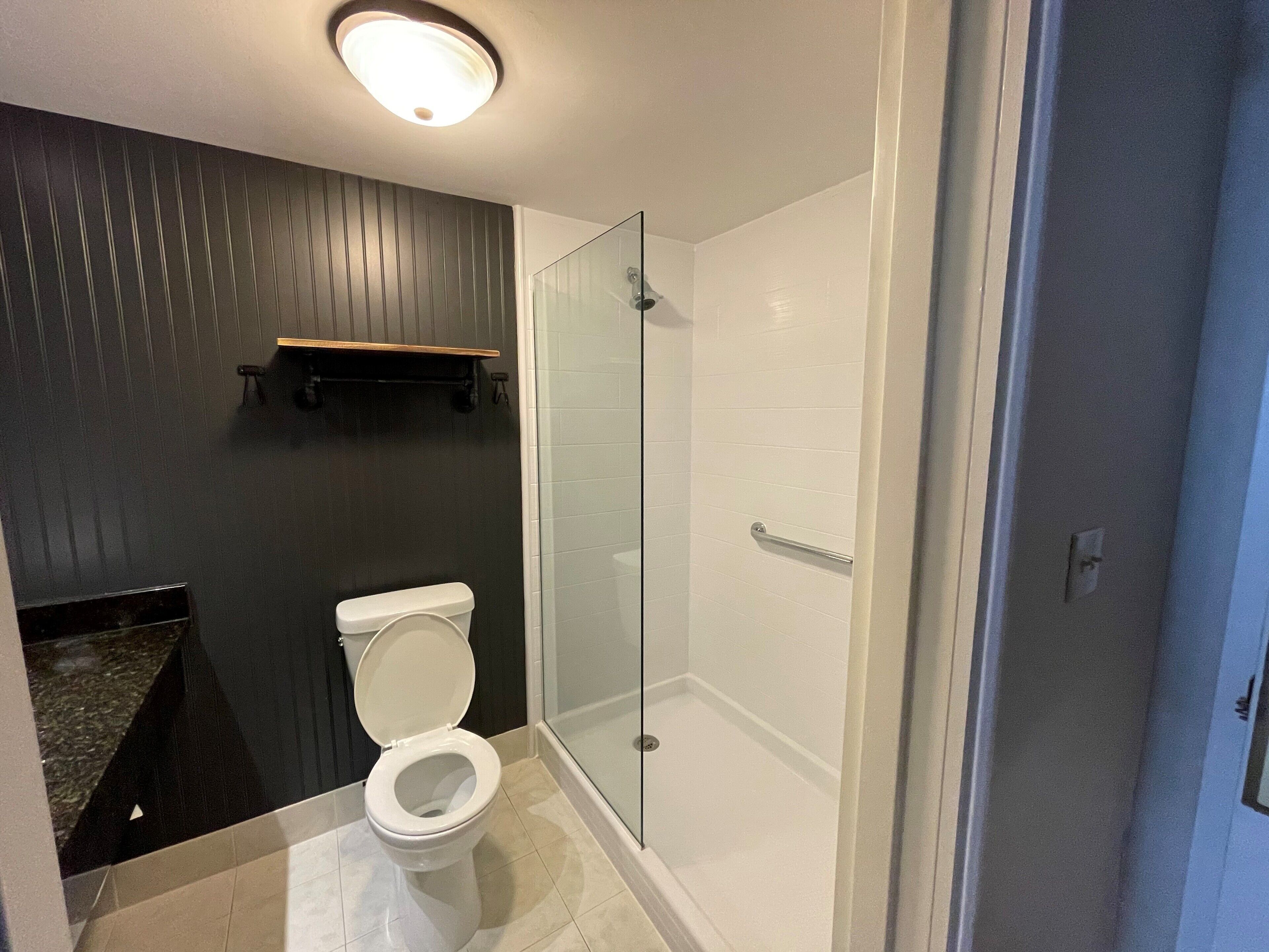 Un baño moderno con inodoro, cabina de ducha de vidrio y pared de paneles de madera oscura.