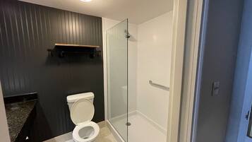 Un baño moderno con inodoro, cabina de ducha de vidrio y pared de paneles de madera oscura.