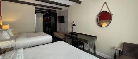 A hotel room with two beds, a desk, a chair, a TV, and a round mirror on the wall.