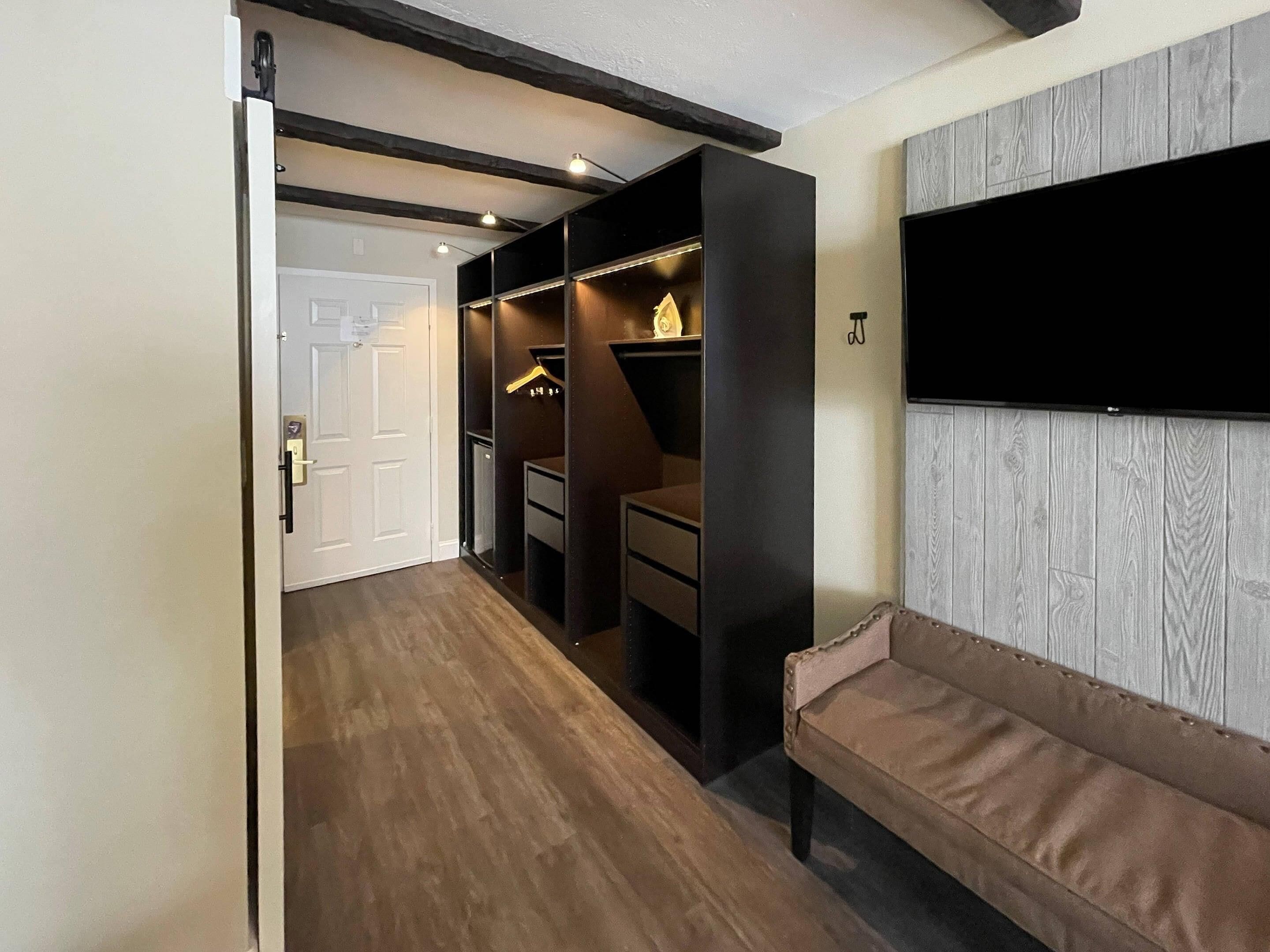 A hallway with a wooden floor, a bench, a wardrobe, and a mounted TV.