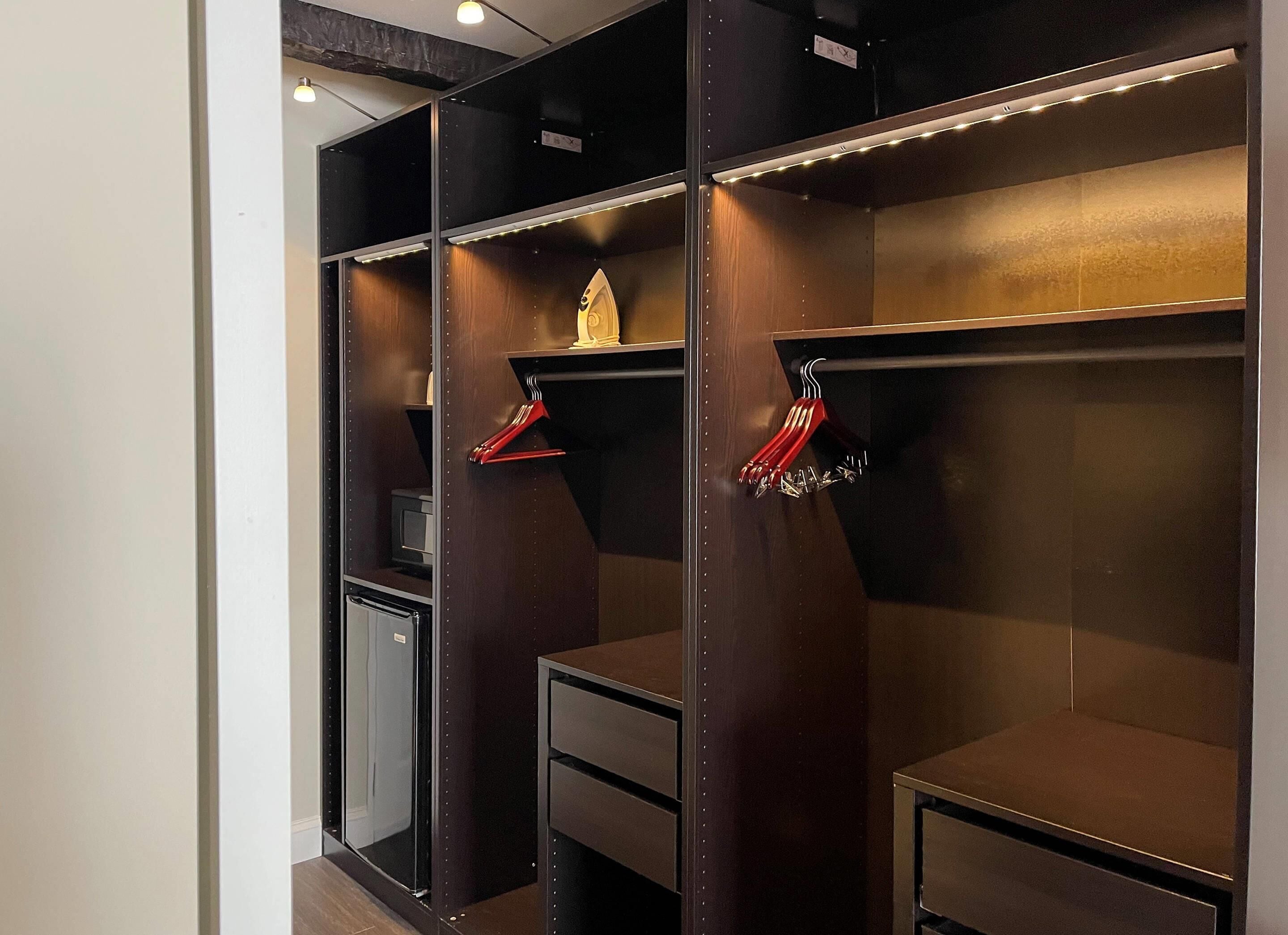Un vestidor con estantes de madera y espacio para colgar ropa, un escritorio pequeño y un espejo.