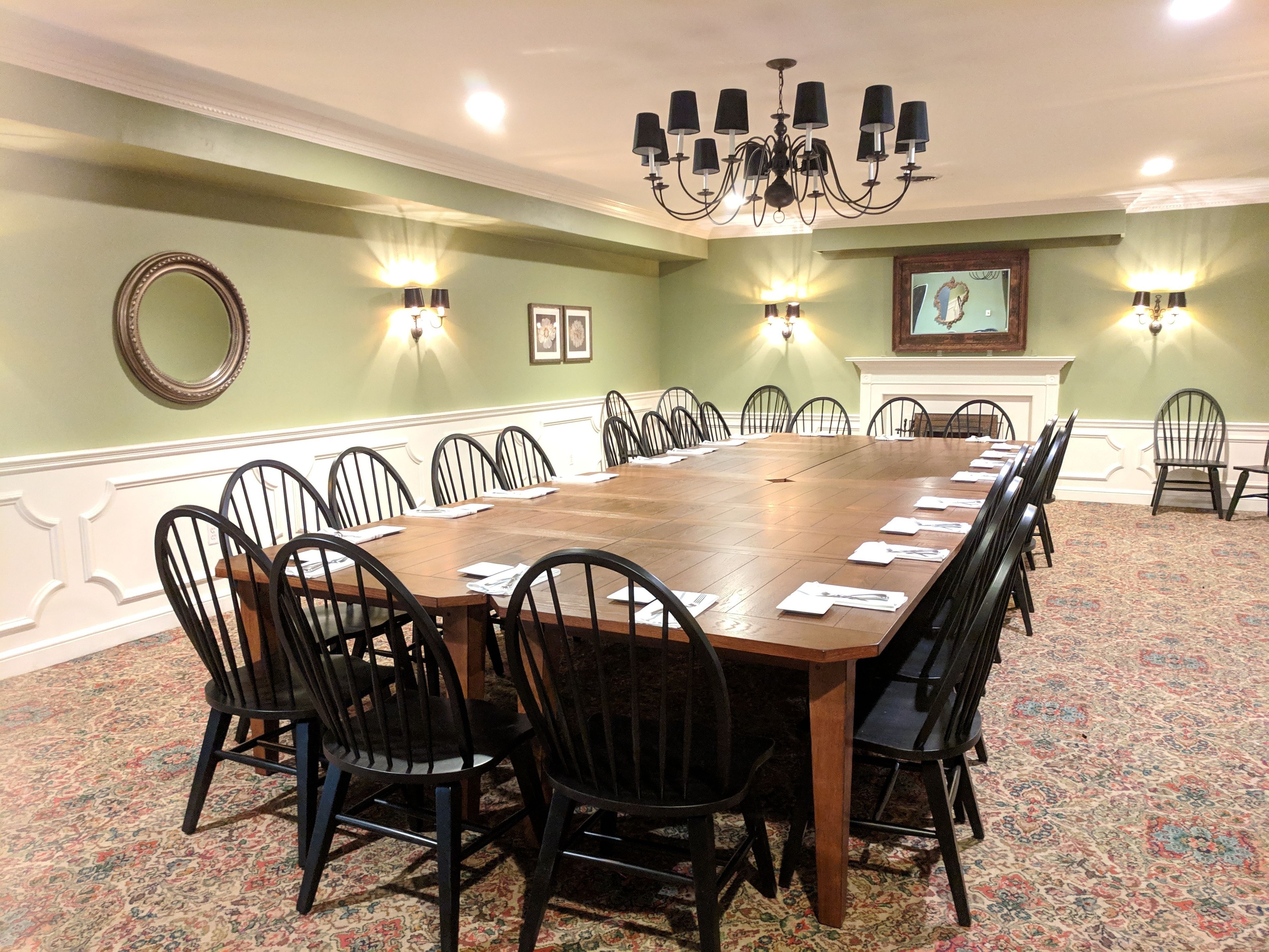 Un salón de conferencias con una larga mesa de madera, sillas negras y un candelabro.