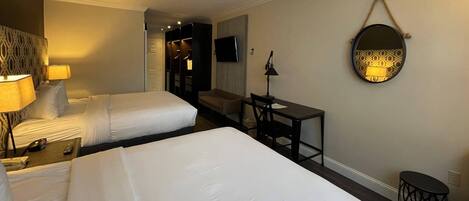 Habitación de hotel con dos camas, un escritorio, una silla, un televisor y un espejo en la pared.