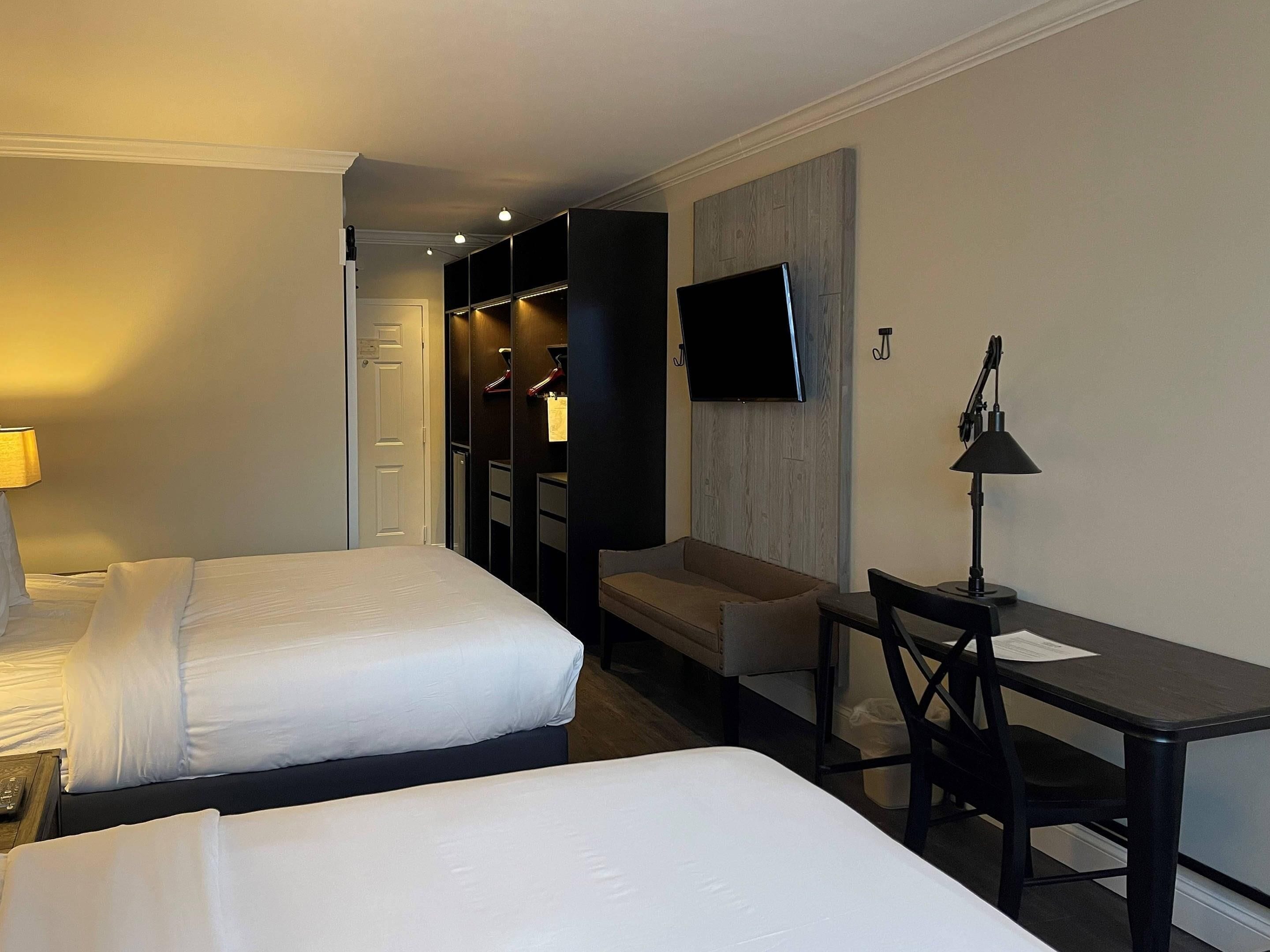 A hotel room with two beds, a desk, a chair, a TV, and a wardrobe.