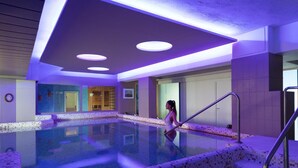 An indoor swimming pool with a tiled edge, a person walking by, and a staircase leading into the pool area. - Hermitage Resort & Thermal Spa (Ischia)