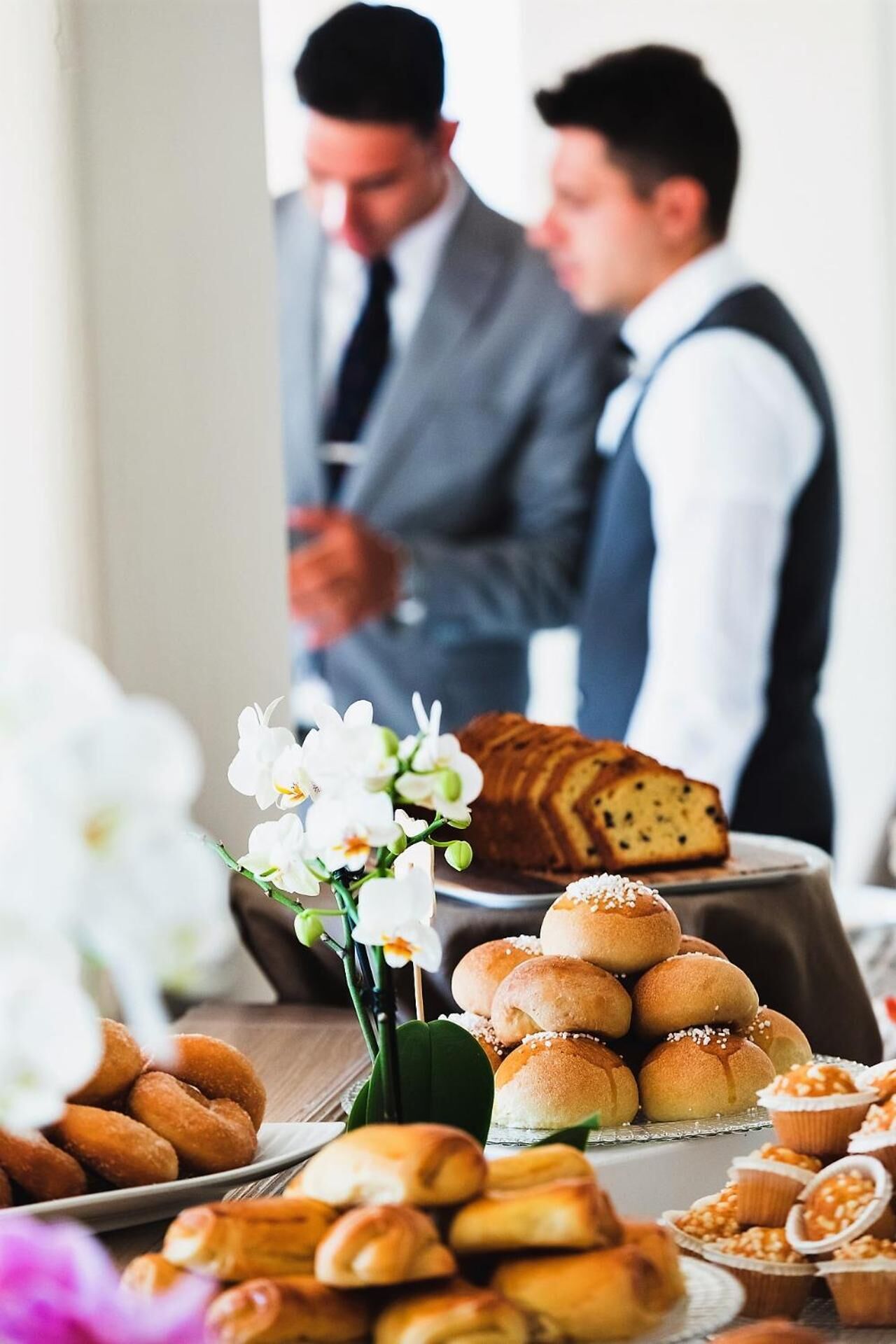A buffet table with various baked goods, including bread and pastries, and a floral arrangement.