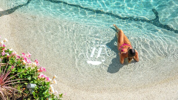 A woman in a bikini standing at the edge of a pool with clear water and a sandy bottom. - Hermitage Resort & Thermal Spa (Ischia)