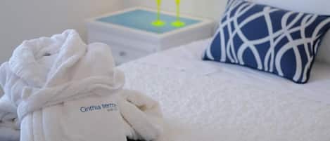 A hotel room with a neatly made bed, a white robe, a blue and white pillow, and a bedside table with two glasses of water.