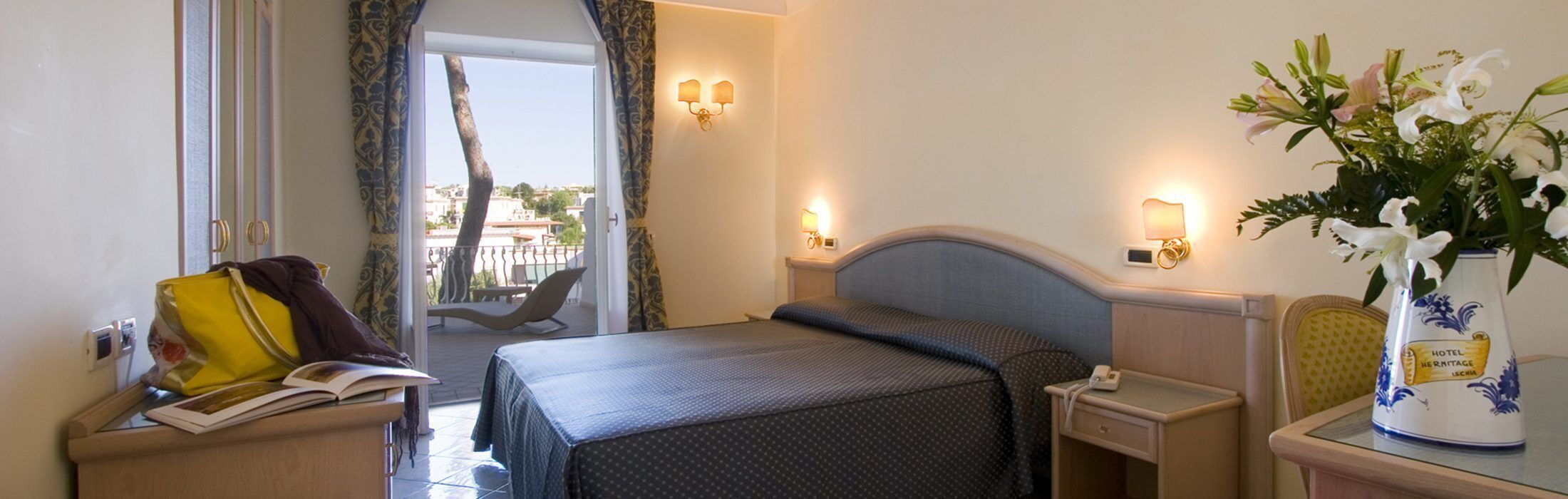 Habitación de hotel con cama, mesita de noche y vistas al exterior.