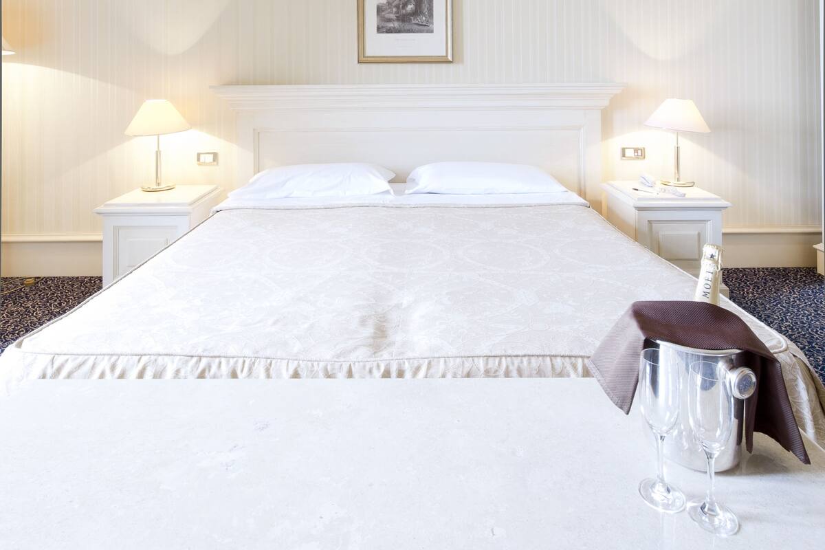 Habitación de hotel con una cama grande, dos mesitas de noche con lámparas, un cuadro enmarcado en la pared y un minibar.