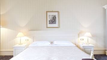 A hotel room with a large bed, two bedside tables with lamps, a framed picture on the wall, and a minibar.