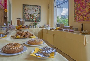 A breakfast buffet with various pastries, fruits, and beverages on a table with a view of greenery outside. - Hotel Relais II Chiostro di Pienza (Pienza)