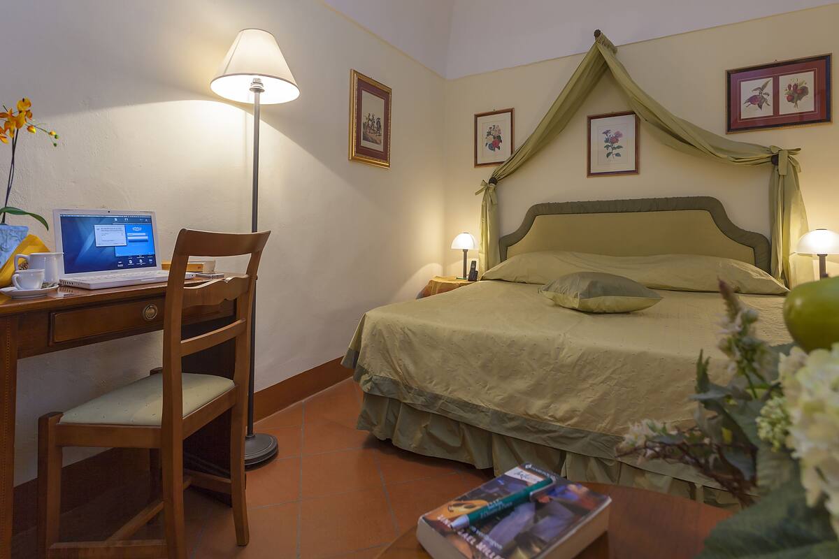 Habitación de hotel con cama, escritorio con computadora portátil, silla y mesita de noche con lámpara.