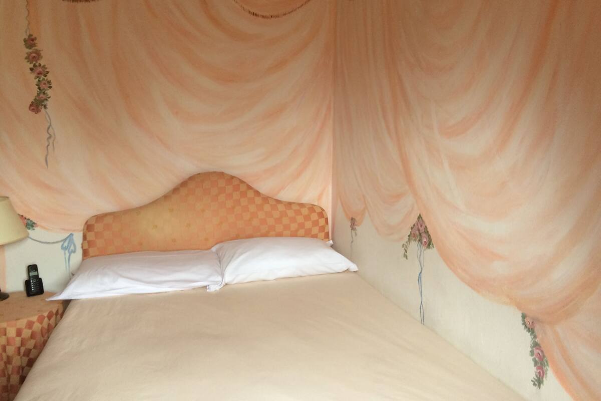 Una cama con cabecera estampada de cuadros, almohada blanca y dosel con motivos florales.