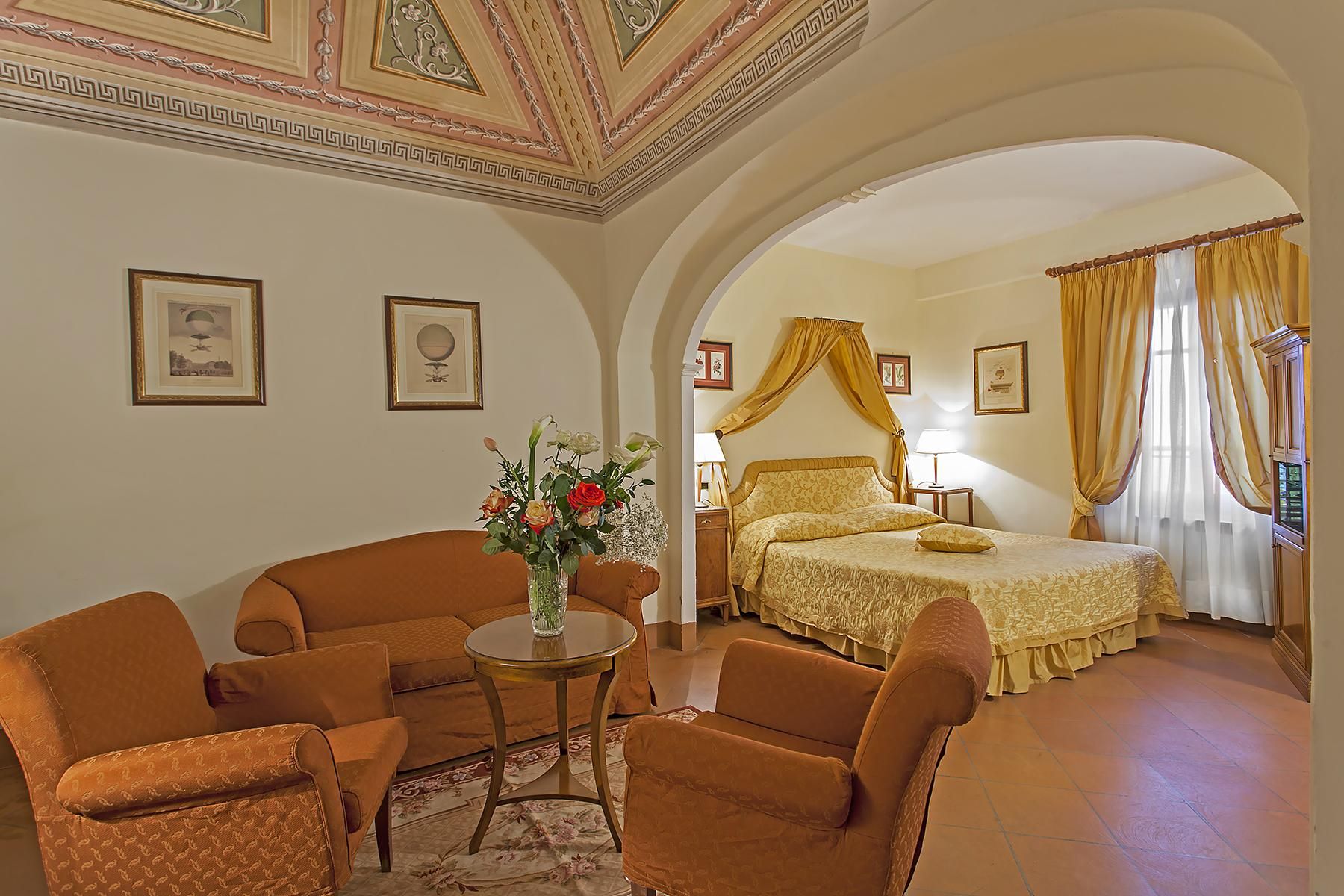 A hotel room with a bed, a sitting area with chairs, a small table, and a vase of flowers.