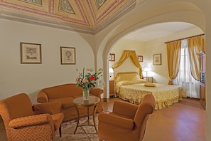 Habitació d'hotel amb un llit, zona de seients amb cadires, una taula petita i un vas amb flors.