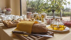 A table with bread, pastries, and oil bottles, set against a window with a view of trees.