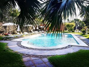 A rectangular swimming pool with a tiled edge, surrounded by a stone pathway, and shaded by palm trees. - Hotel Villa Paradiso dell'Etna (San Giovanni la Punta)
