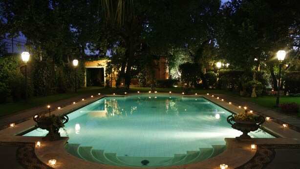 A swimming pool surrounded by a garden with trees and a building in the background. - Hotel Villa Paradiso dell'Etna (San Giovanni la Punta)