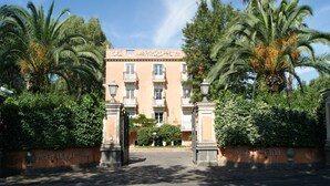 A hotel entrance with a wrought iron gate, palm trees, and a clear sky. - Hotel Villa Paradiso dell'Etna (San Giovanni la Punta)