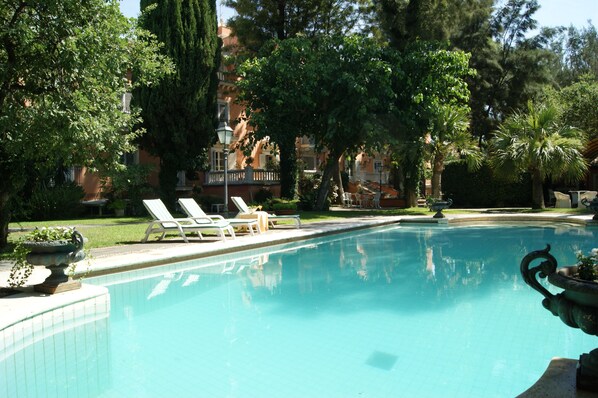 A swimming pool with lounge chairs, surrounded by trees and a building with balconies. - Hotel Villa Paradiso dell'Etna (San Giovanni la Punta)