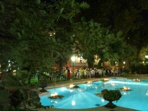 Une vue nocturne d’une piscine entourée d’arbres et agrémentée d’espaces de détente en plein air.