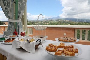 A buffet table with various dishes, a bottle of sauce, and a view of a mountainous landscape. - Hotel Villa Paradiso dell'Etna (San Giovanni la Punta)