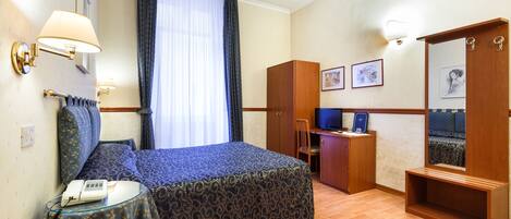 A hotel room with a bed, a desk, a chair, a small table with a phone, and a mirror.