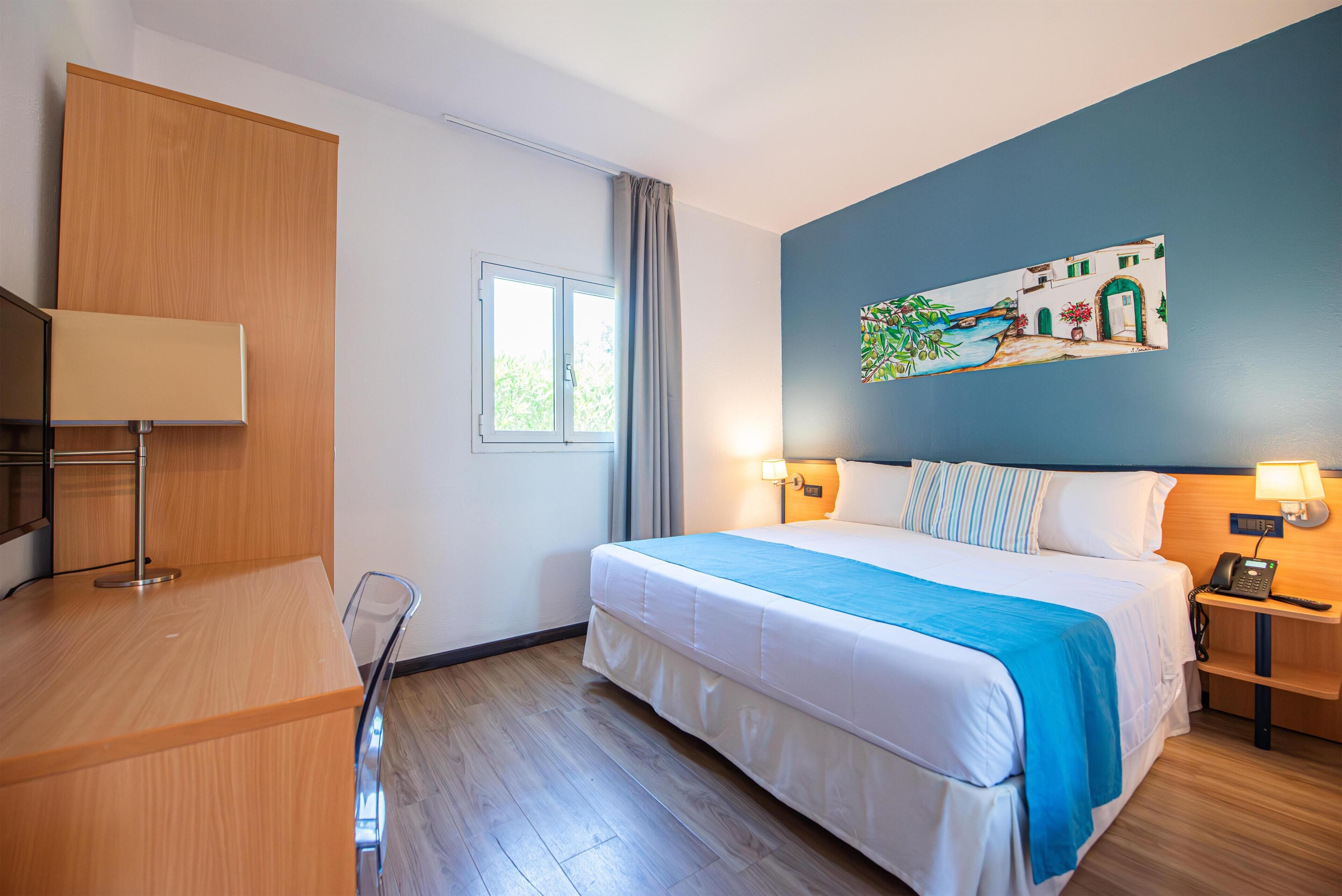Habitación de hotel con cama, mesitas de noche, escritorio, silla, ventana y un cuadro en la pared.