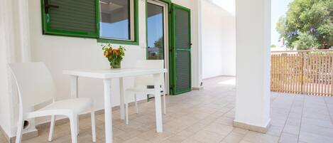 A clean, white interior with a table and chairs, a small vase with flowers, and green shutters on the windows.