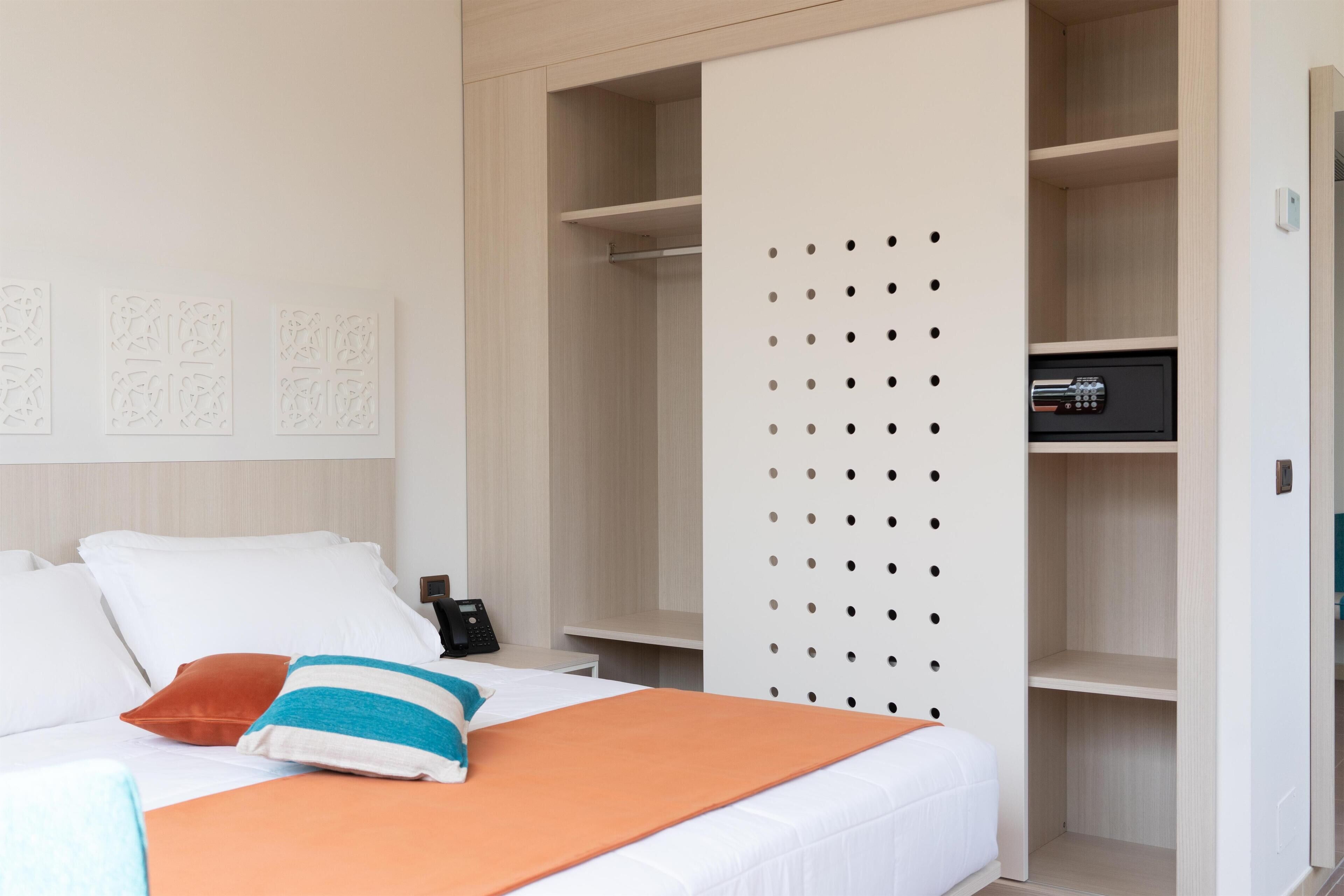 Una habitación de hotel con una cama, un armario y una mesita de noche con un teléfono.