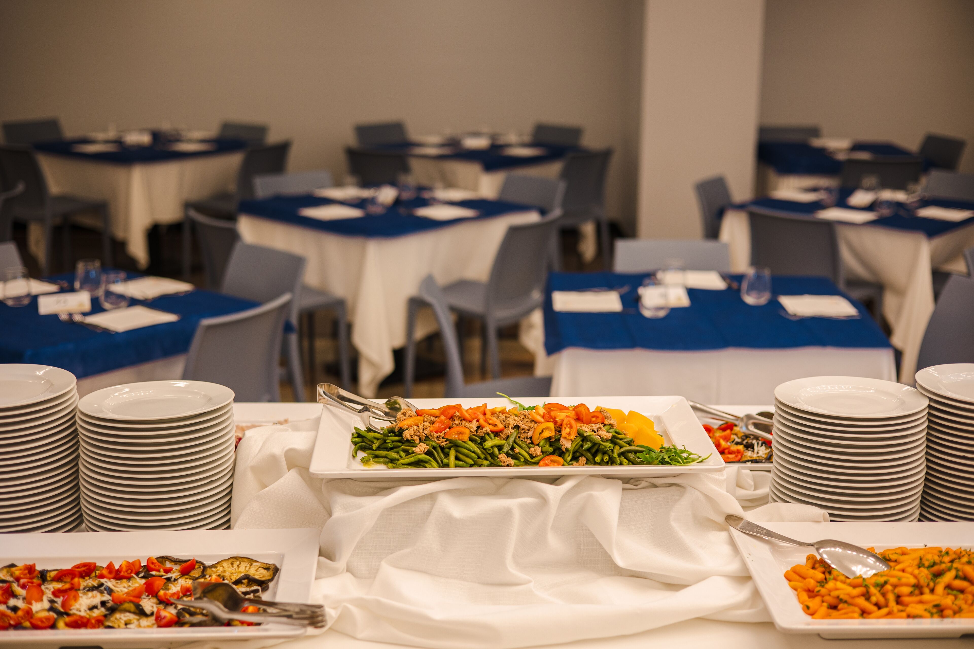 Ein Buffet mit mehreren Tischen, jeweils mit einer blauen Tischdecke und darunter weißen Tischdecken.