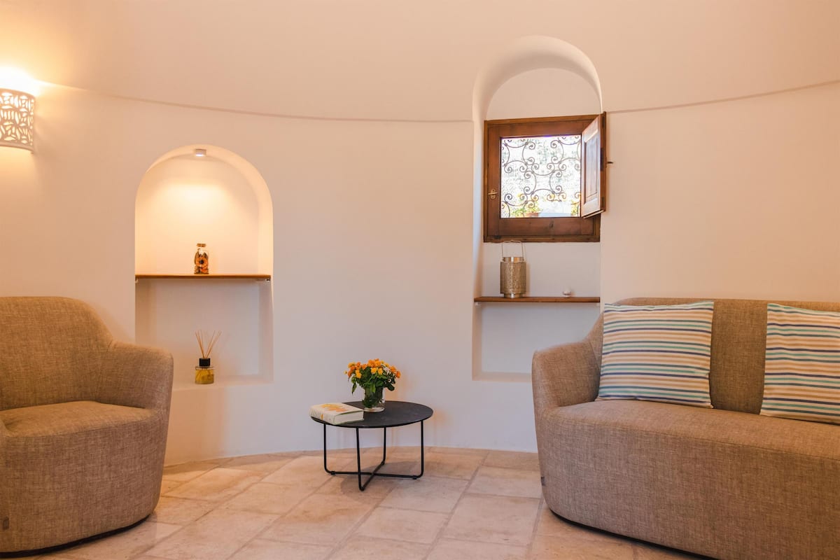 A cozy living room with two sofas, a small round table with a vase of flowers, and a window with decorative ironwork.
